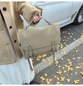 Detail of khaki frosted tote bag with metal ring handle and decorative straps on street
