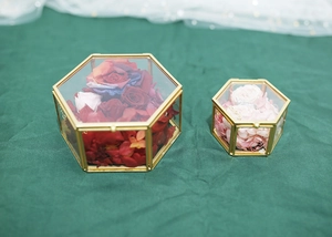 Detail of hexagonal glass ring boxes with gold metal frames and red preserved roses