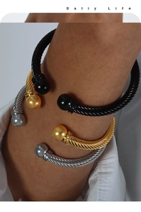 Dettaglio di bracciali a corda intrecciata in oro, argento e nero sovrapposti al polso