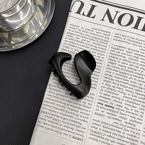 Detail of matte black irregular claw clip with organic curves on a newspaper background