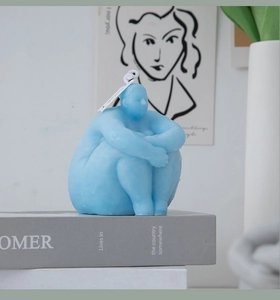 Artistic blue female torso scented candle on a decorative book in a minimalist setting