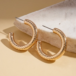Detailed macro view of golden C-shaped hoop earrings with textured dotted surface