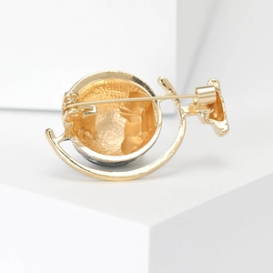 Back view of gold globe brooch showing secure pin fastener on white geometric cubes