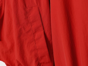 Detail shot of the side pocket stitching on a red nylon jacket with woven texture