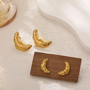 Detail showing golden croissant earrings with textured finish on a wooden display stand