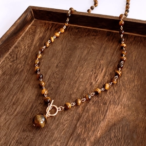 Detailed view of a tiger eye stone necklace with a large bead pendant and golden OT buckle