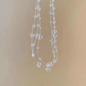 Detail of multi-layer beaded necklace featuring clear irregular crystals on transparent cord