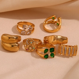 Multiple gold plated stainless steel rings with green gemstones on beige fabric background