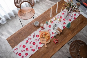Detail of Christmas table runner featuring red candy and festive ball prints on white fabric