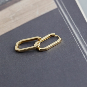 Macro detail of polished gold-plated rectangular silver earrings on textured background