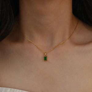 Détail d'un collier doré avec pendentif en zircon vert carré porté par un mannequin