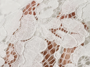 Detail of white hollow-out floral lace fabric with intricate crochet and stand collar texture
