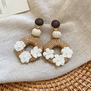 Detail of bohemian rattan earrings with white fabric flowers and dark wood studs