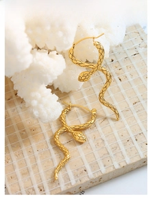 Detailed close-up of golden snake earrings with textured scales on white coral stand