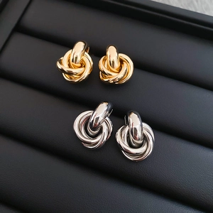 Detailansicht der verschlungenen Knoten-Ohrstecker in Gold und Silber auf schwarzem Tablett
