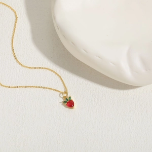 Exquis collier en or doté d'un pendentif fraise rouge sur une surface blanche texturée