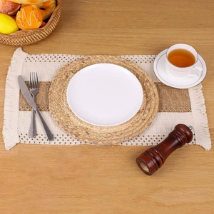 Detail of woven table mat set with beige fringes and spiral patterns on a wooden table