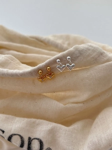 Macro shot of silver and gold heart stud earrings with zircons on linen fabric