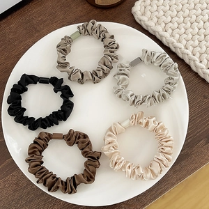 Set of 5 glossy satin silk scrunchies in neutral tones displayed on a white plate