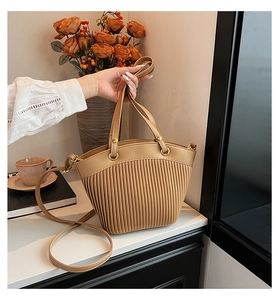 Detail of khaki pleated bucket bag with gold hardware in a warm lifestyle setting
