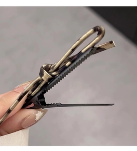 Close-up of golden metal duckbill hair clip with vintage woven knot design detail