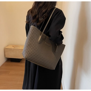 Detail view of dark grey woven PU leather tote bag worn by model in minimalist setting
