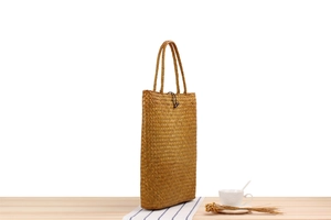 Detail of woven straw beach bag with handles on wooden table with dried flowers