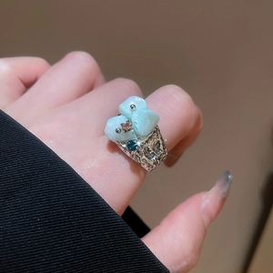 Detailed view of an irregular silver floral ring with light blue stones on a finger