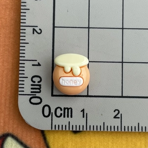 Detailed macro view of a 1cm mini bee honey jar resin charm on a grid ruler mat