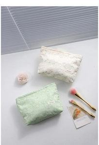 Detailed close-up of floral jacquard makeup bags in cream and light green on a desk