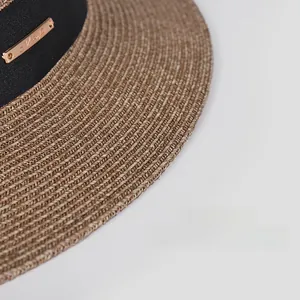 Detailed macro view of woven straw sun hat brim with black ribbon and gold metal plate