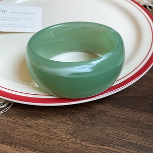 Close-up of a wide green acrylic marble bangle placed on a ceramic plate with wood backdrop