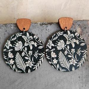 Close-up of bohemian round wooden earrings with white floral patterns on black background
