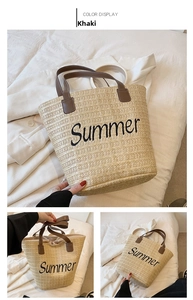 Close-up of khaki straw woven tote bag featuring black Summer embroidery and leather handles