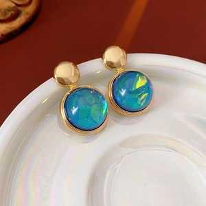 Close-up of round resin earrings with iridescent blue-green stones on a pearly plate
