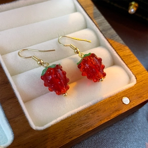 Macro shot of realistic strawberry drop earrings with red glass texture and golden hooks