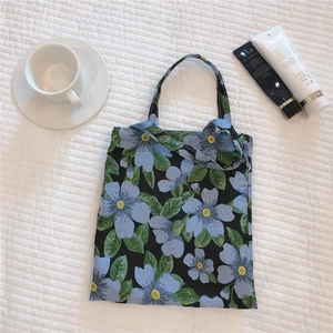 Flat lay of floral canvas tote bag with light blue flowers on black fabric background