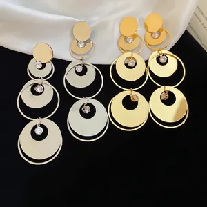 Polished gold and silver tiered round dangle earrings with zircon crystals on dark background