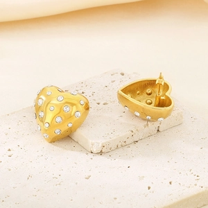 Gros plan de boucles d'oreilles cœur dorées avec cristaux sur pierre texturée