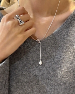 Close-up of bow knot silver necklace with pearl pendant on grey knitted sweater background