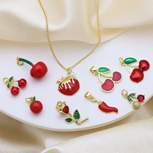 Fashionable gold necklaces with red enamel cherry, apple and chili pendants on silk background