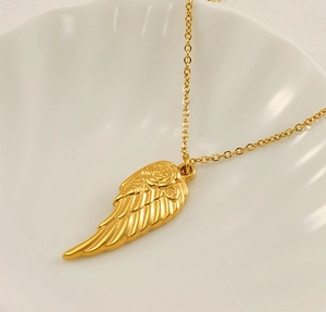 Detailed shot of 18K gold angel wing pendant with rose relief on a white shell base