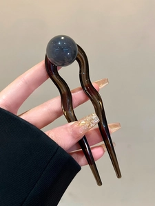 Détail d'une épingle à cheveux en U ondulée en résine brune avec une perle bleue