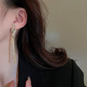 Gros plan de boucles d'oreilles pendantes feuille or et argent portées avec un tailleur noir
