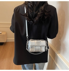 Détail du sac bandoulière argenté tressé avec bandoulière chaîne sur un blazer noir chic
