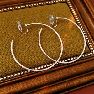 Dettaglio di orecchini a cerchio argento opaco testurizzato con clip in cornice vintage