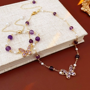Macro view of butterfly charms with purple amethyst beads and white pearls on golden chains