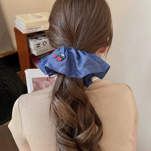 Detailed view of a blue denim scrunchie with red cherry embroidery worn by a model
