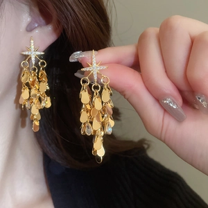 Gros plan de boucles d'oreilles étoile dorées avec zircons et sequins pendants sur modèle