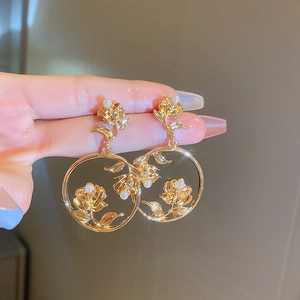 Close-up of golden metal rose earrings featuring delicate pearls and starry lighting